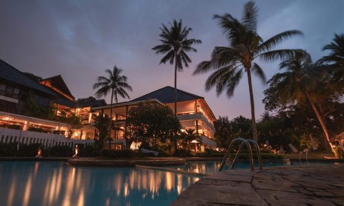 Luxurious tropical resort with swimming pool and palms at dusk, perfect for a tranquil vacation.